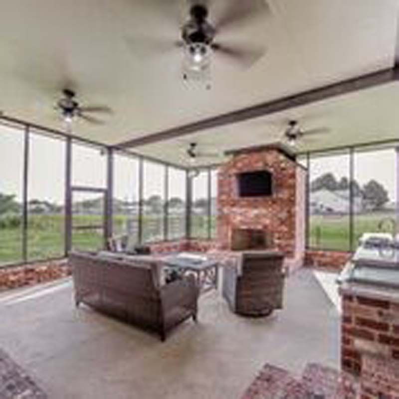 Screened outdoor patio with brick fireplace, ceiling fans, and seating overlooking a green yard