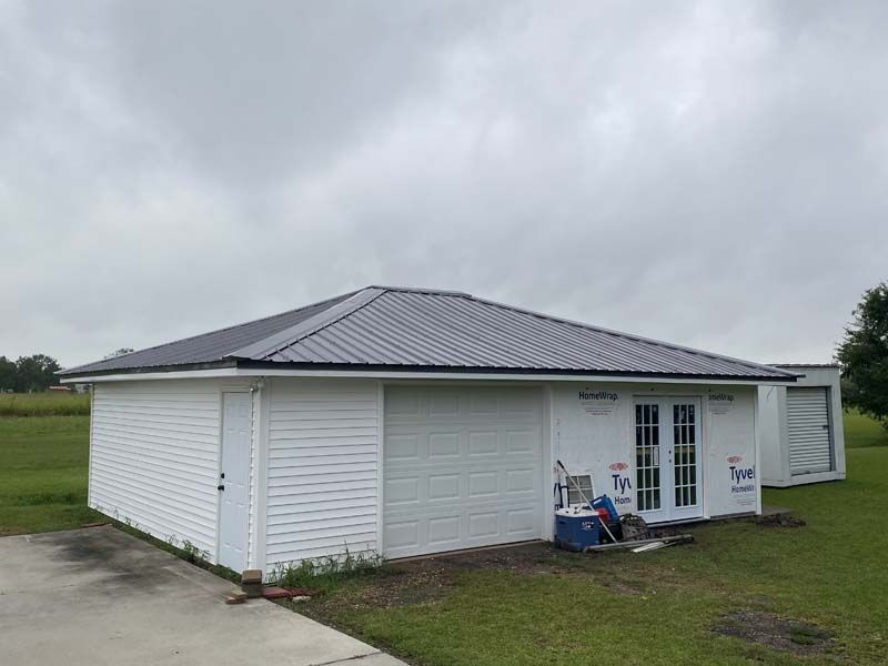 White single-story house with a gray roof and front porch, set on a grassy lot under cloudy skies