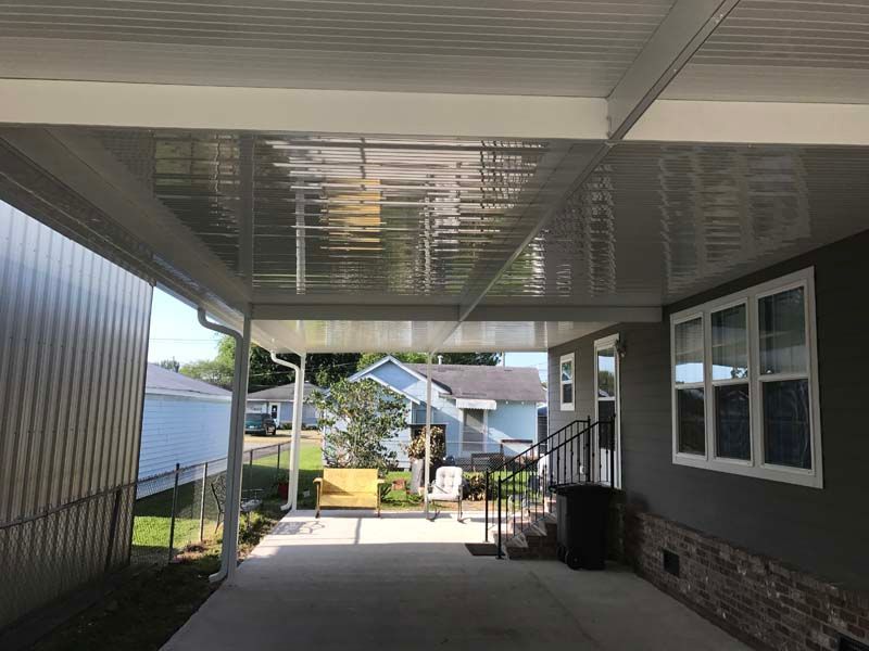 Covered carport with white ceiling, concrete floor, and a view of a house and yard beyond.