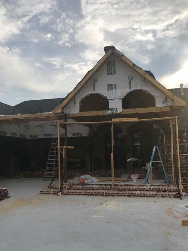 House under construction with ladders, scaffolding, and exposed brick on the front porch.