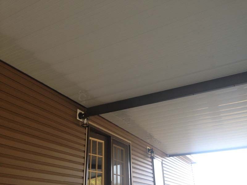 Covered porch ceiling with brown siding and a windowed door corner against a cloudy sky