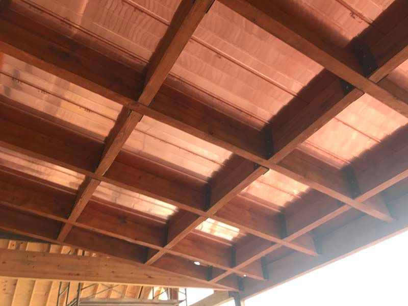 Wooden ceiling with exposed beams and reddish panels, viewed from below indoors.