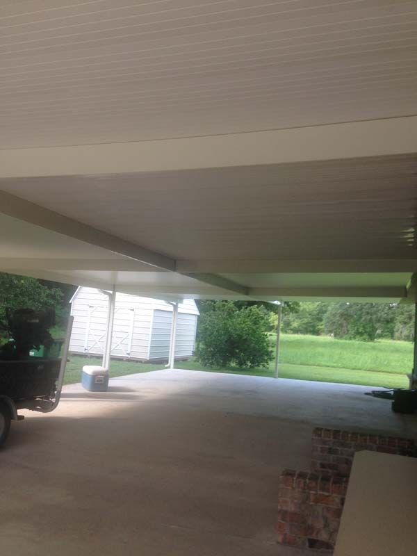 Covered concrete patio with white siding, brick steps, and a view of a green lawn and trees.
