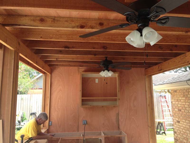 Wooden covered patio with ceiling fans; person in yellow shirt working on a table at left.