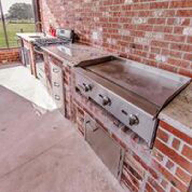 Outdoor brick patio with built-in stainless steel grill and countertop under a covered area