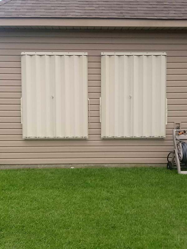 Two white shuttered windows on a beige house above a green lawn