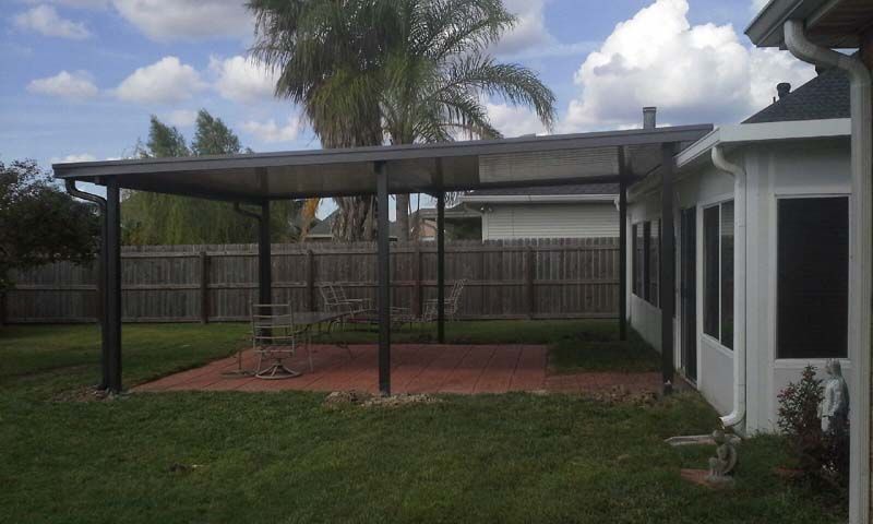 Backyard patio with a covered pergola, brick pavers, grass, fence, and house exterior.