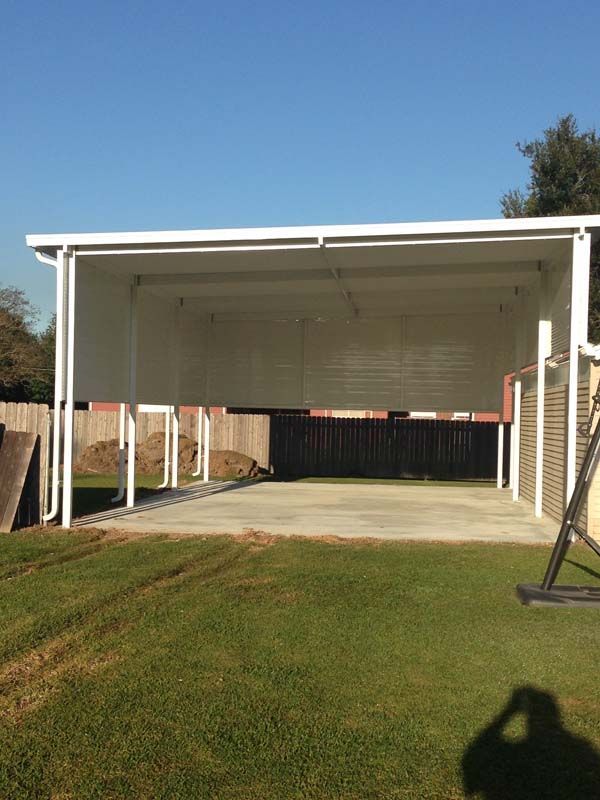 White carport with concrete driveway and green lawn under a clear blue sky