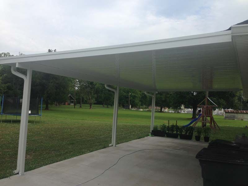 Covered pavilion with white columns beside a grassy park and trees