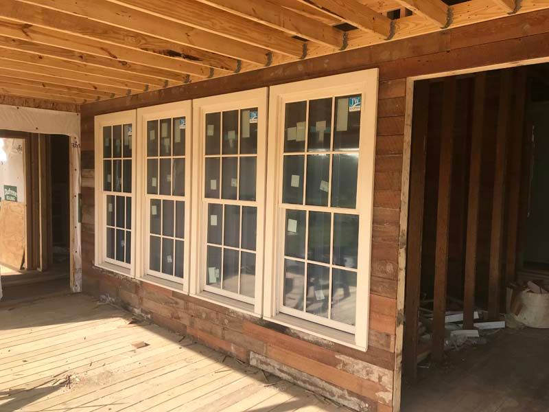 White-framed windows and a brick wall under a wooden porch roof, with unfinished wooden siding.