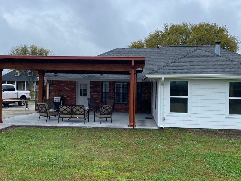 Single-story white house with a covered porch, brick wall, patio furniture, and grassy yard