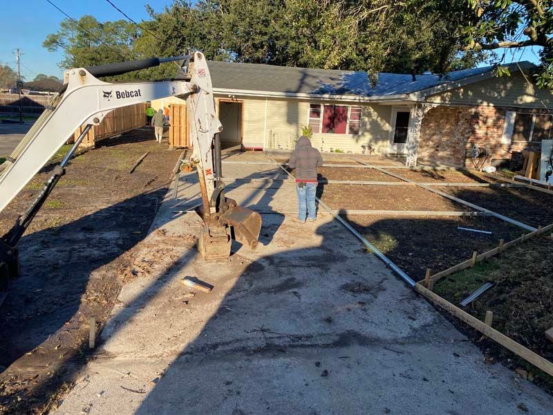 Construction crew working on a driveway beside a house, with an excavator and exposed ground.
