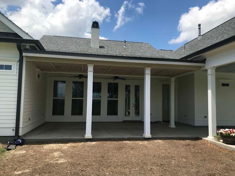 Covered front porch of a white house with columns and double doors under a gray roof.