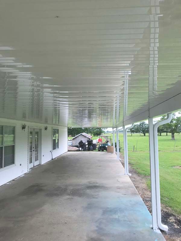 Covered walkway with white ceiling and columns beside a building and grassy lawn.