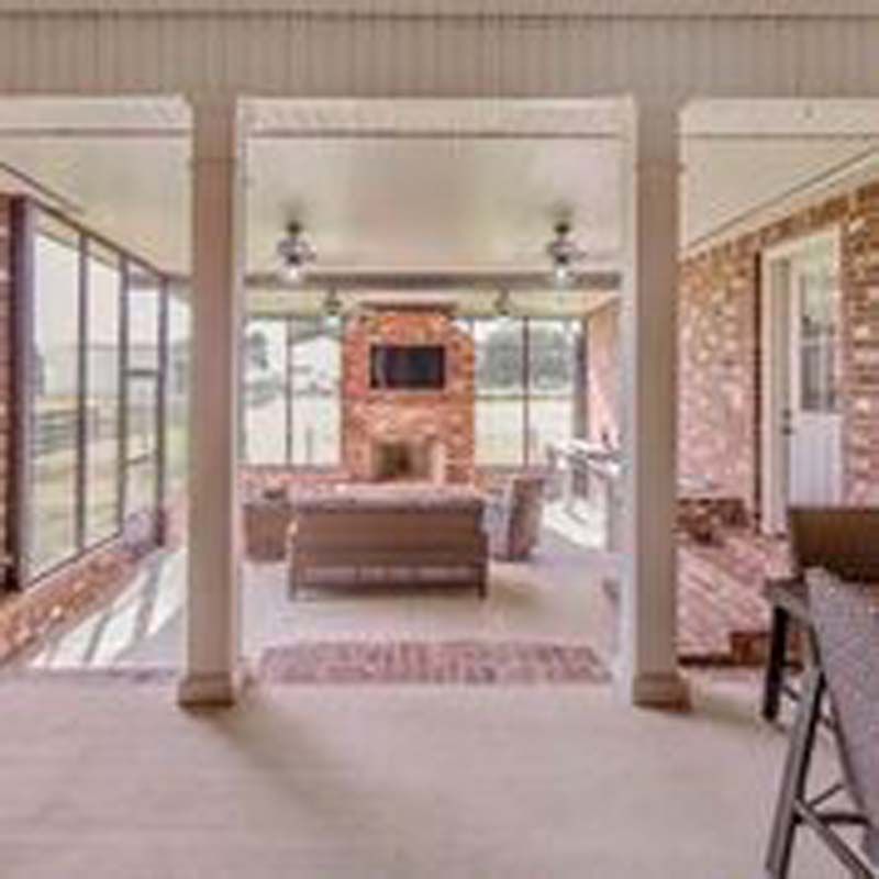 Spacious covered patio with brick fireplace, wicker sofa, and large windows overlooking a yard