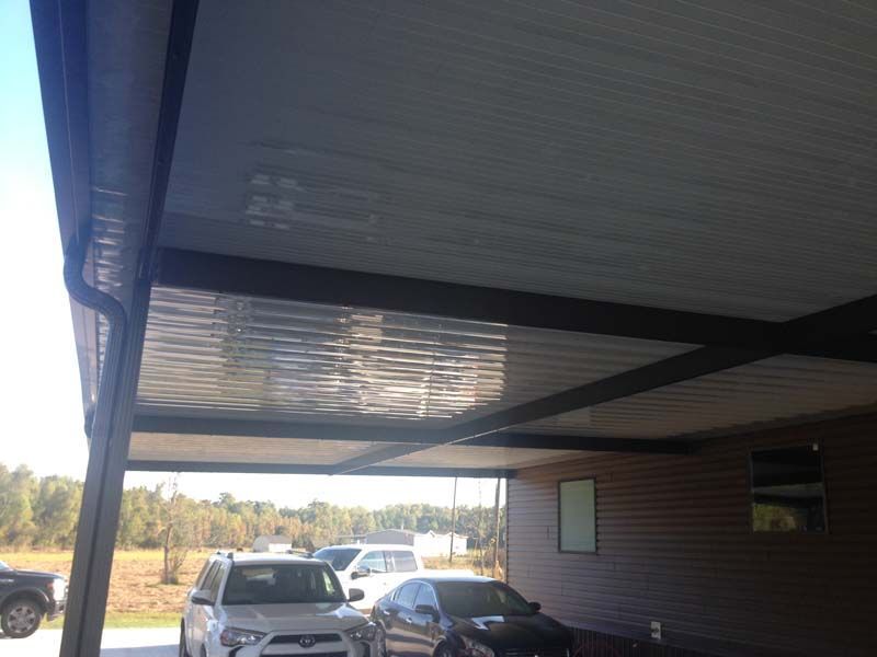 Covered driveway with parked cars and a house exterior on a sunny day