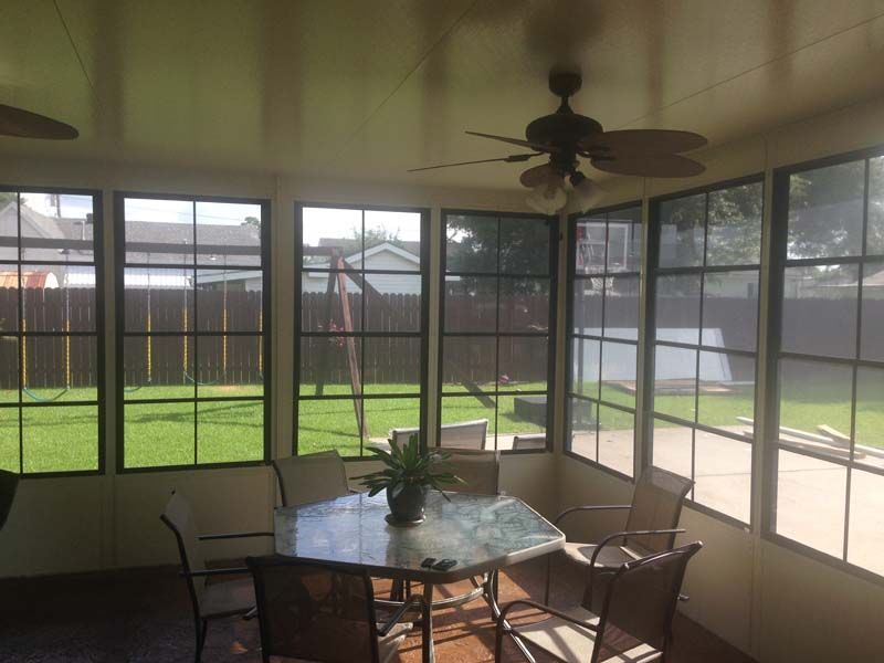 Screened porch with glass table, chairs, potted plant, ceiling fan, and backyard view.