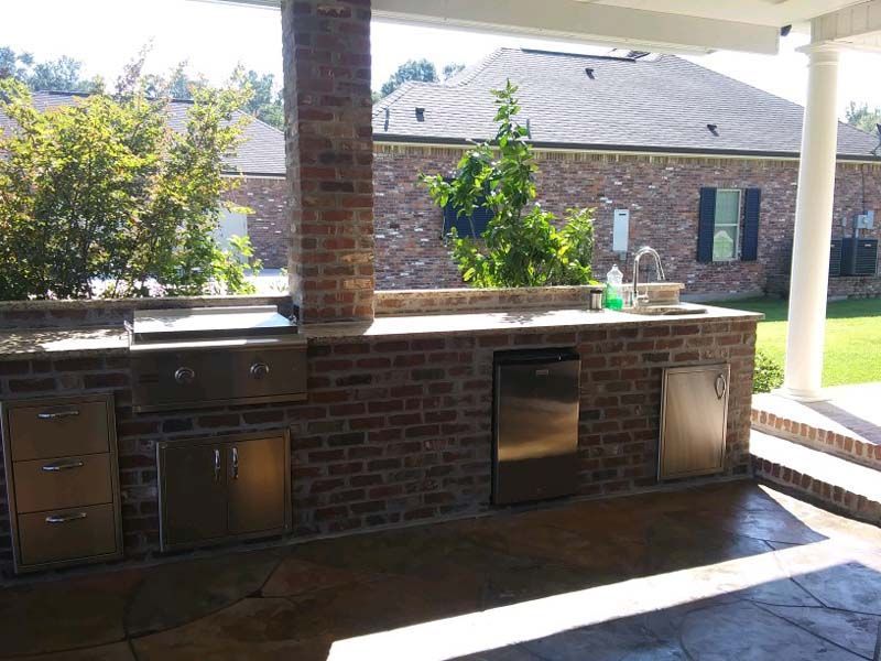 Covered outdoor brick grill and counter area with built-in stainless steel cabinets and sink