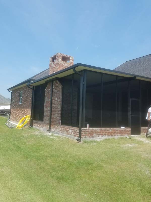 Backyard view of a brick house with a screened porch and grassy lawn under a blue sky