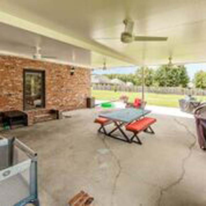 Covered patio with brick wall, ceiling fans, picnic table, and outdoor seating overlooking a yard