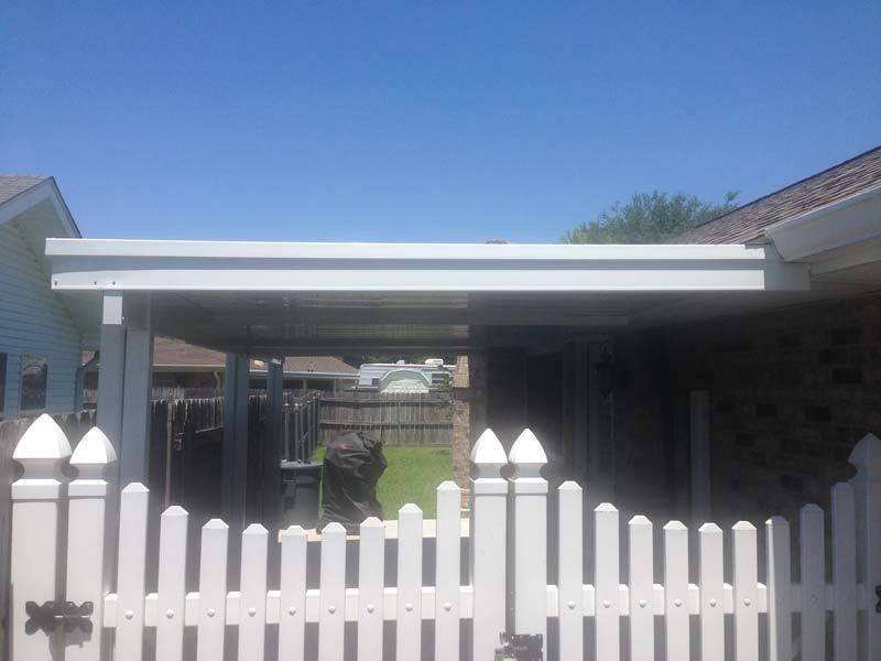 White picket fence with a carport and brick house under a clear blue sky