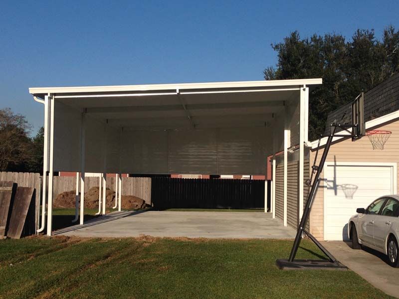 Open-sided carport with a concrete floor and a parked car beside it under a clear blue sky.