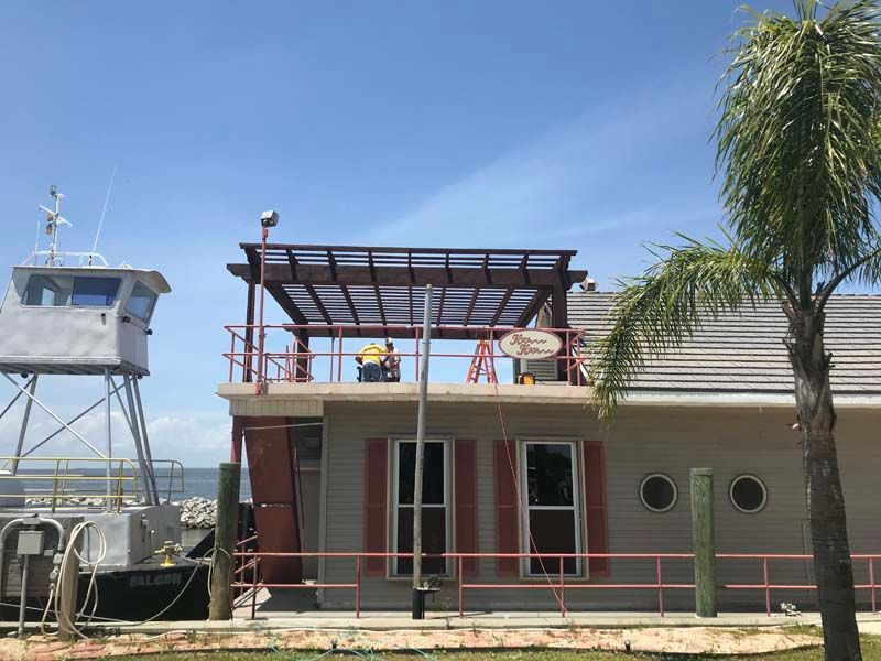 Workers on a rooftop pergola above a waterfront building under a clear blue sky