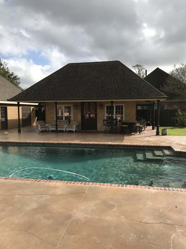 Backyard pool with a house, covered patio, and cloudy sky