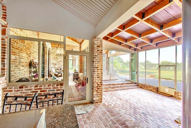 Bright sunroom with brick walls, glass windows, and a tiled floor overlooking a lake.