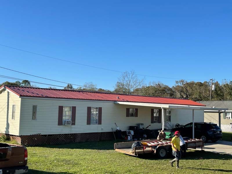 Single-story house with red roof, parked vehicles, and a person standing in the yard under a clear blue sky