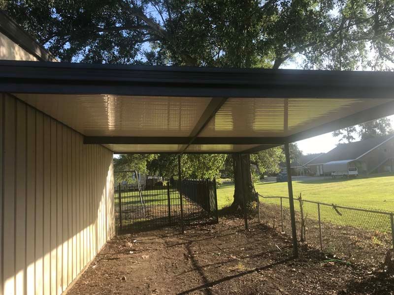 Covered chain-link dog pen beside a barn, with a tree and grassy yard beyond