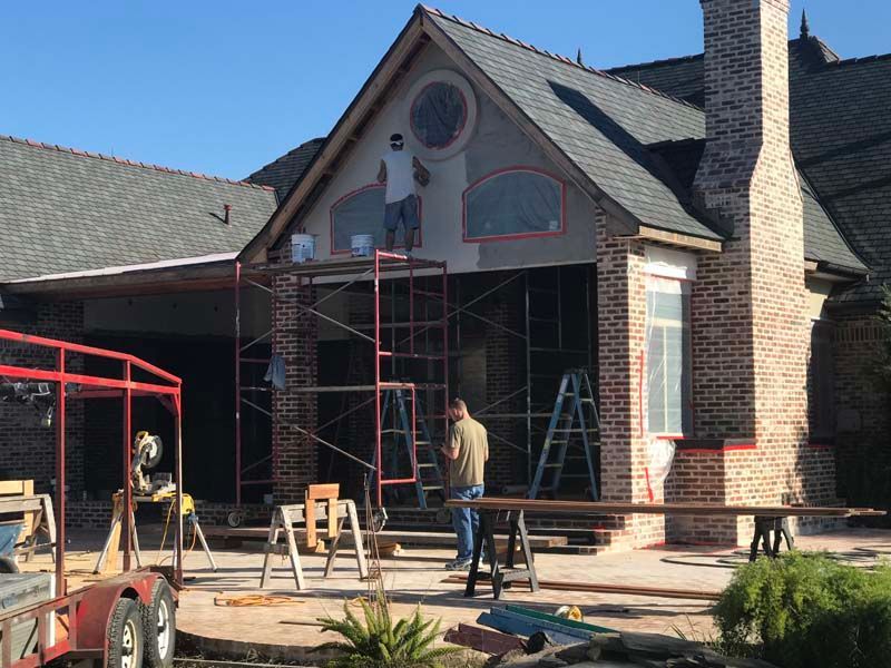 Workers and ladders outside a brick house under renovation with scaffolding over the front porch