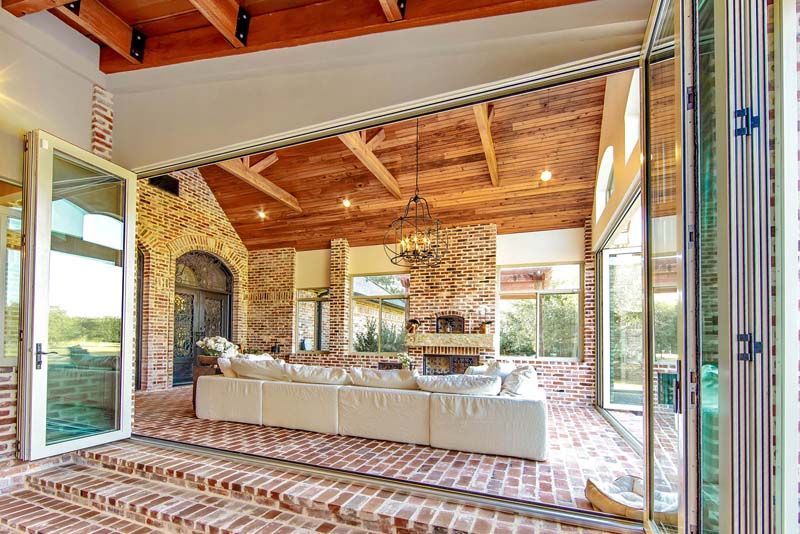 Open living room with stone fireplace, exposed wood beams, and large glass doors opening to a patio.