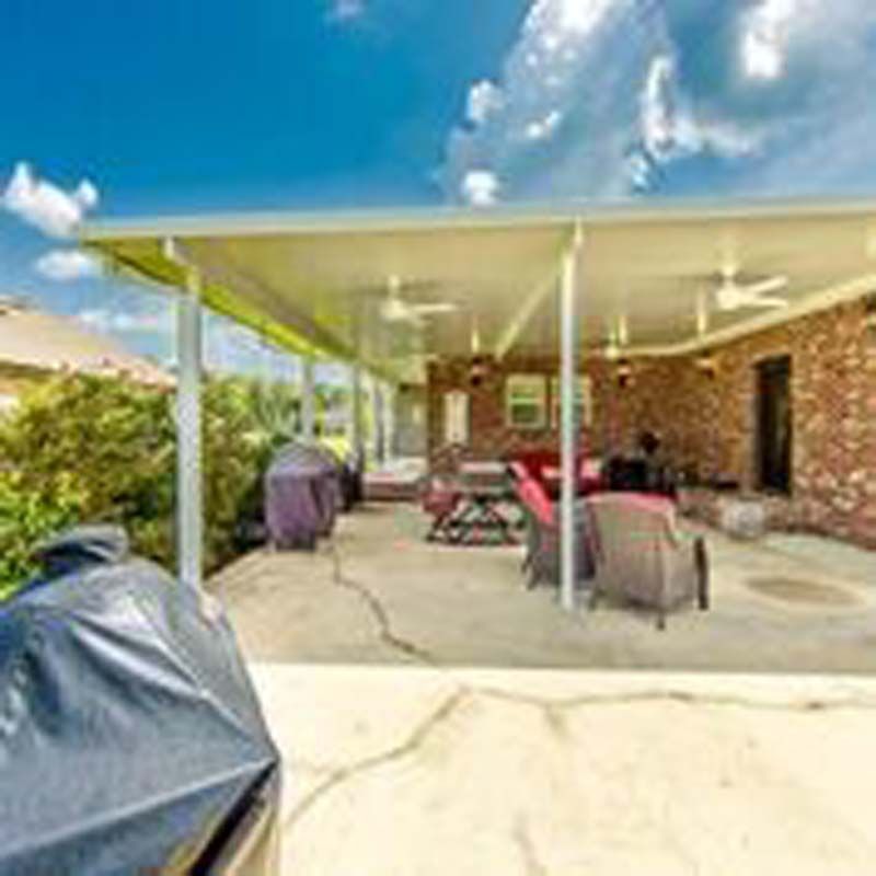 Covered patio with brick wall, outdoor chairs, grill, and a concrete floor under a blue sky