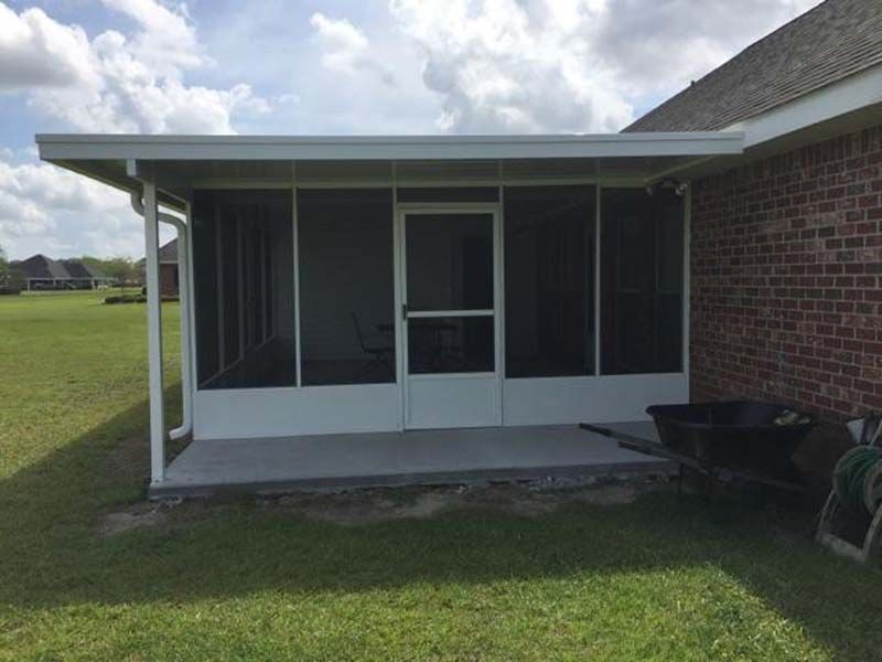 Screened porch attached to a brick house beside a grassy yard