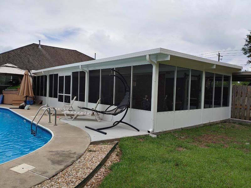Screened patio enclosure beside a backyard pool with white frame and black chairs on the deck