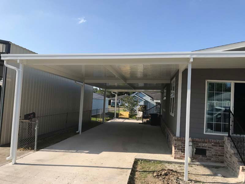 Covered carport beside a gray house with a concrete driveway and stairs leading to a side door