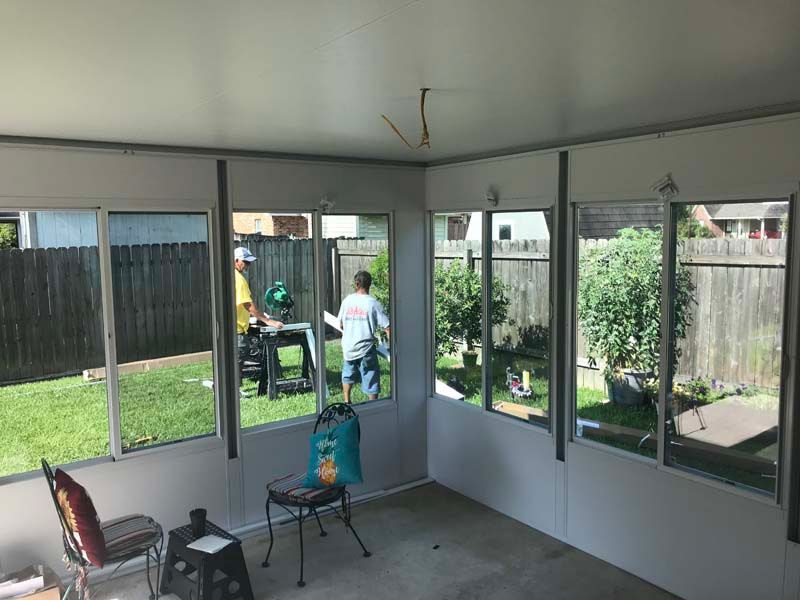 Sunroom with glass walls, chairs, and a small table; two people stand outside in the garden.