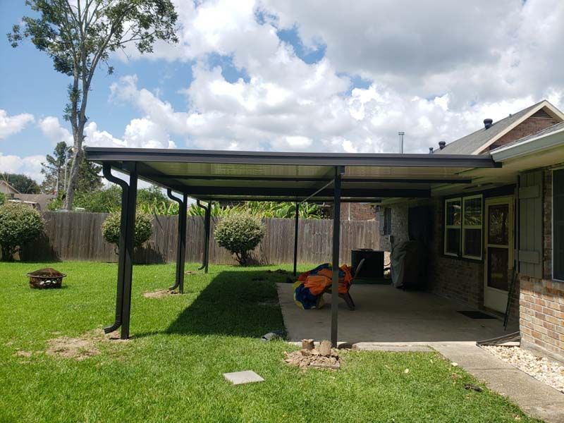 Backyard patio with covered carport, lawn, and a brick house under a cloudy sky