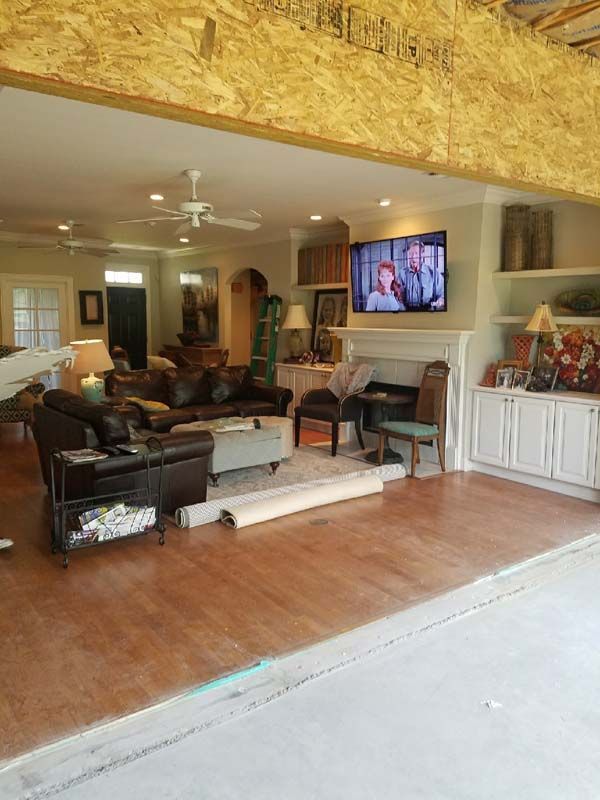Open living room with wooden floor, exposed beam, leather chairs, and a wall-mounted TV.