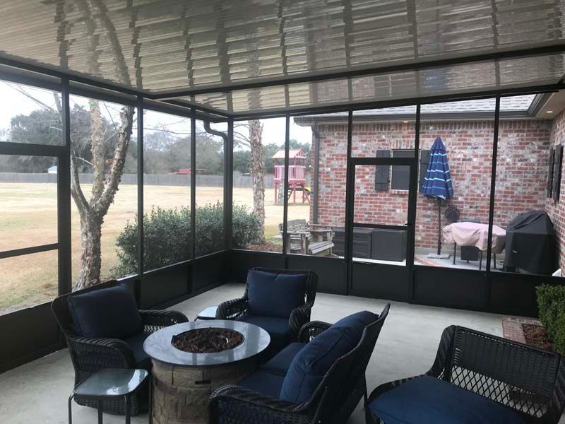 Covered patio with black chairs, round table, grill, and screened view of yard and brick house