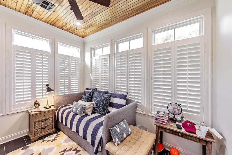 Bright bedroom with white shutters, striped daybed, wood ceiling, and small side tables