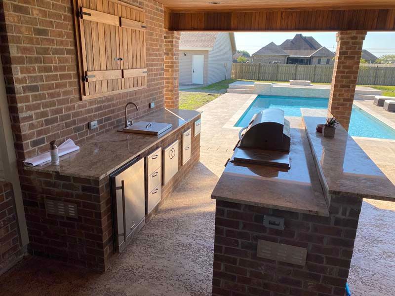 Covered outdoor kitchen by a backyard pool with brick counters and a grill.