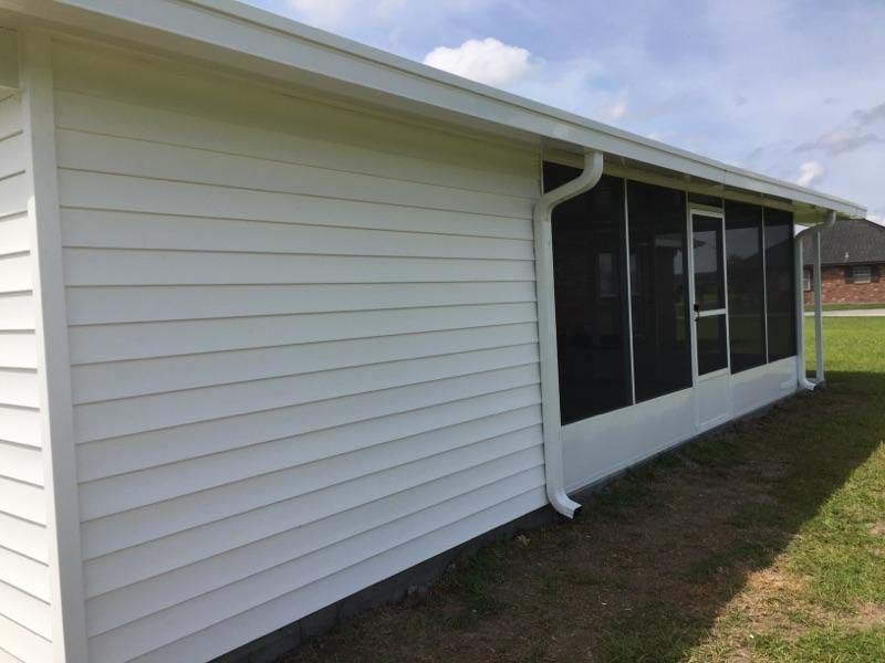White siding on a house exterior with screened windows and a rain gutter along the roofline