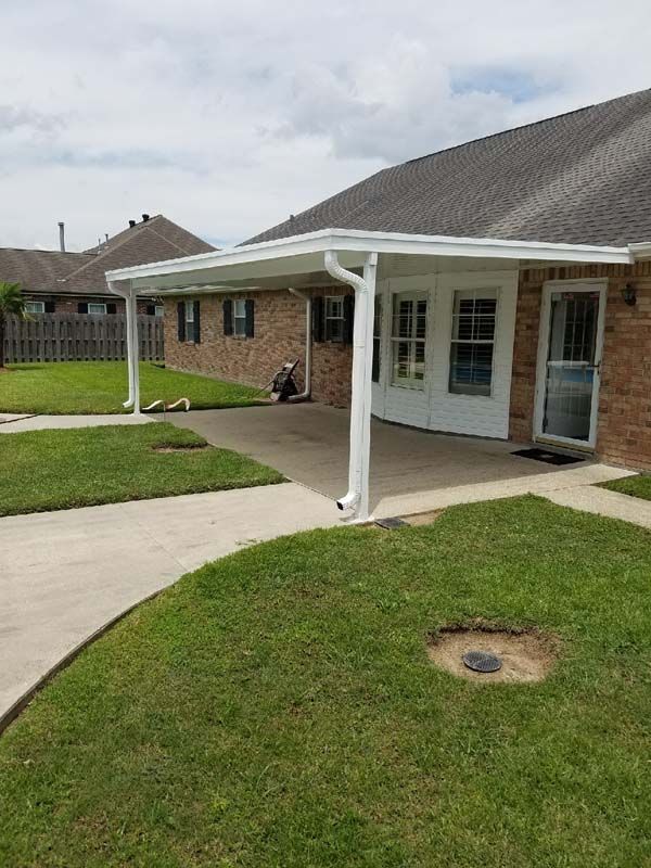 Single-story house with a white covered patio, brick exterior, lawn, and concrete walkway under a cloudy sky