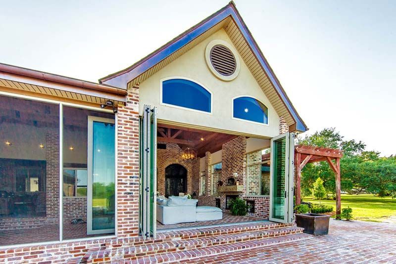Brick house porch with white columns, large windows, and a landscaped yard under a blue sky