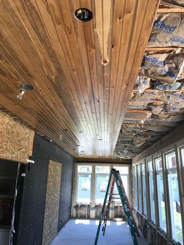 Narrow room under renovation with wood ceiling, exposed insulation, windows, and a ladder in the center.