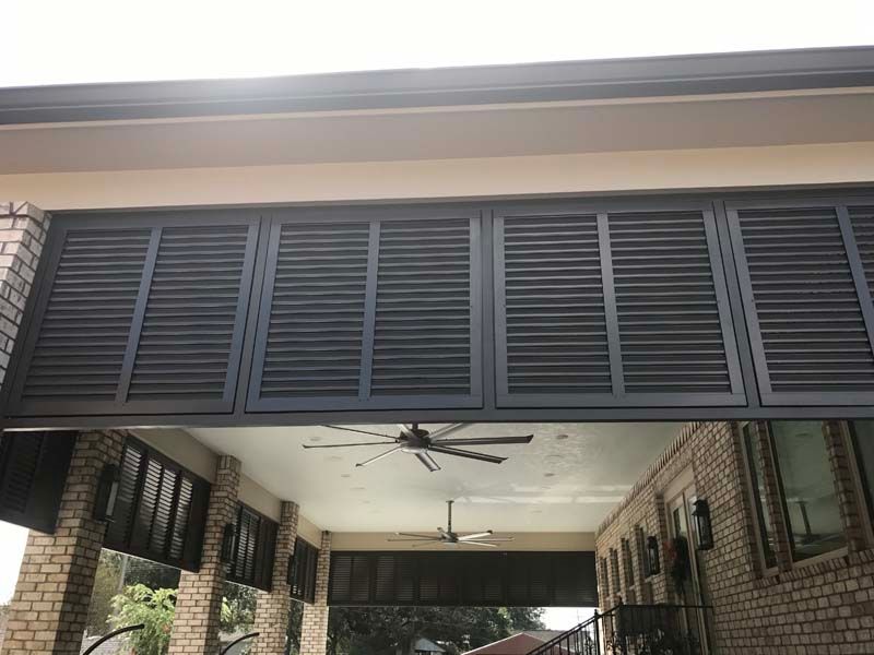 Covered porch with brick walls, ceiling fan, and dark louvered shutters above the entry.