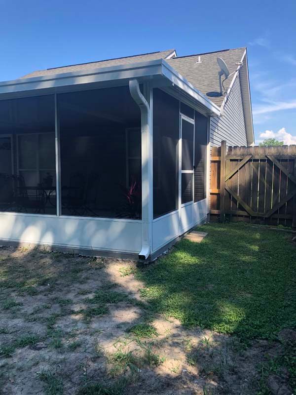 Screened porch on a blue house with a white roof and fenced backyard in sunlight