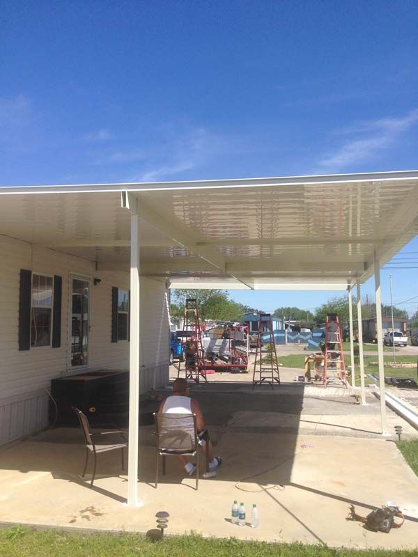 Covered patio beside a house with outdoor furniture, tools, and a view of a backyard and street beyond.